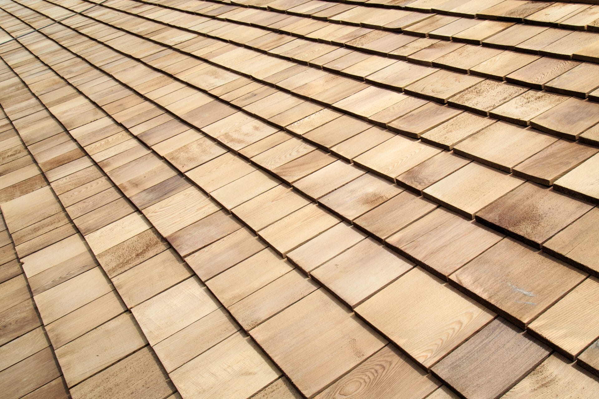 A close-up view of a wooden shingle roof, showing overlapping rows of rectangular, light brown wooden shingles arranged in a neat, uniform pattern. - RoofZen, Chester County PA Roofing, Siding and More