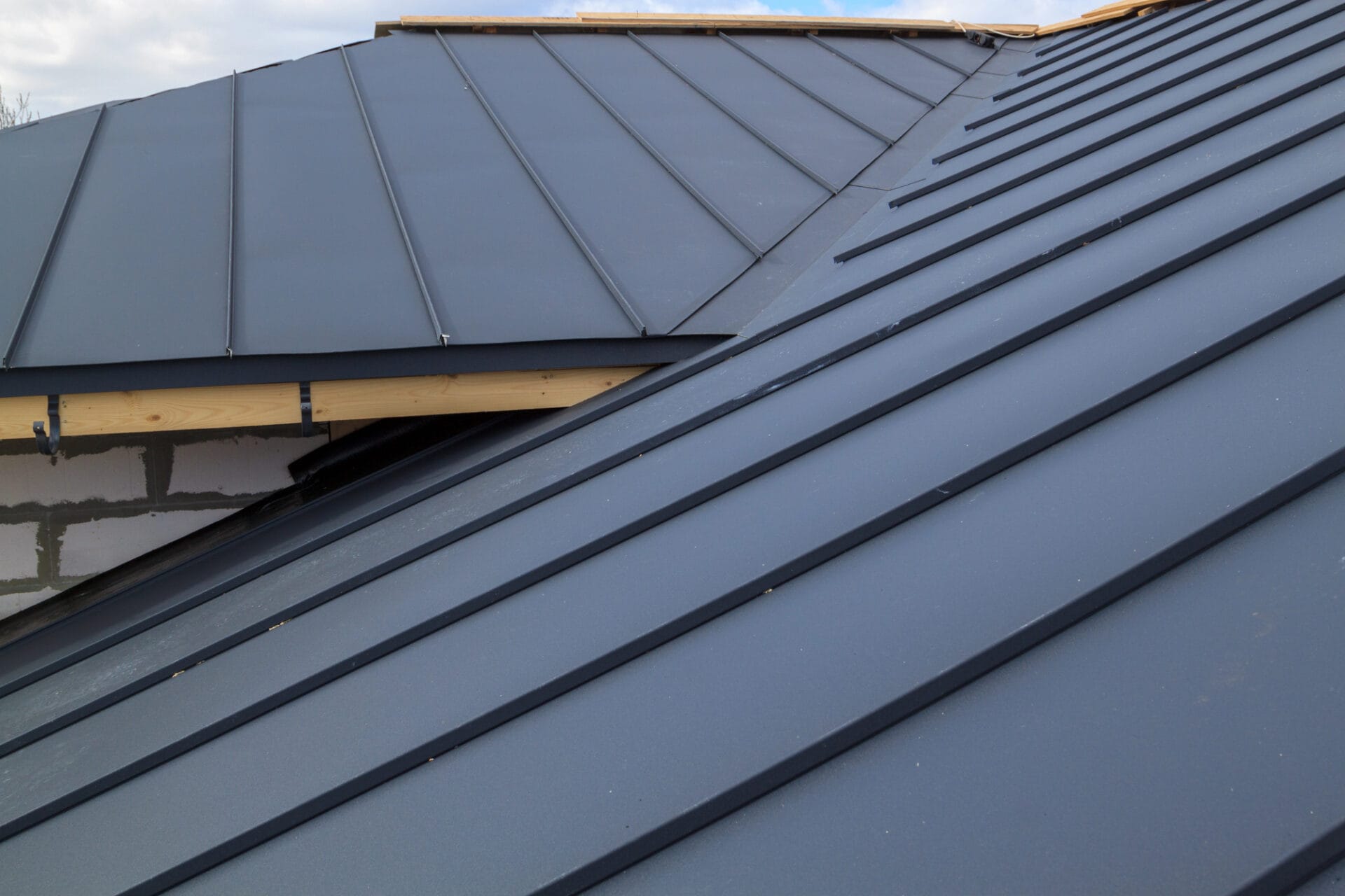 Close-up view of a modern metal roof with standing seam panels and clean lines, showing part of the roof structure and an unfinished wall beneath the eaves. - RoofZen, Chester County PA Roofing, Siding and More