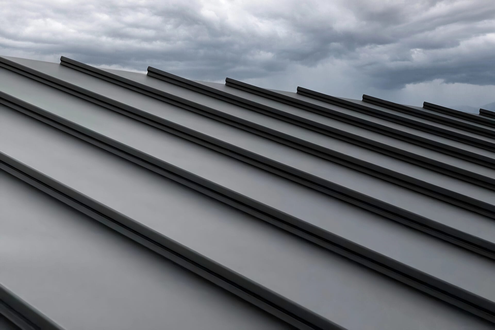 Close-up view of a metal standing seam roof with dark, parallel ridges under a cloudy, overcast sky. - RoofZen, Chester County PA Roofing, Siding and More